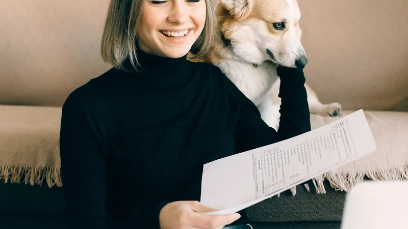 Femme souriante lisant un document à la maison, son chien blanc et roux appuyé contre son épaule - comprendre la franchise d'une assurance pour chien